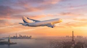 Avion de ligne blanc en vol entre la Statue de la Liberté (New York) et la Tour Eiffel (Paris) au coucher du soleil.